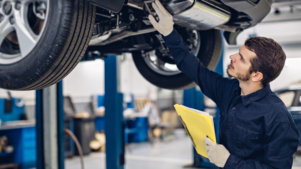 In einer Autowerkstatt-Service. Ein Mechaniker steht unter einem Auto auf der Hebebühne und untersucht das Auto.