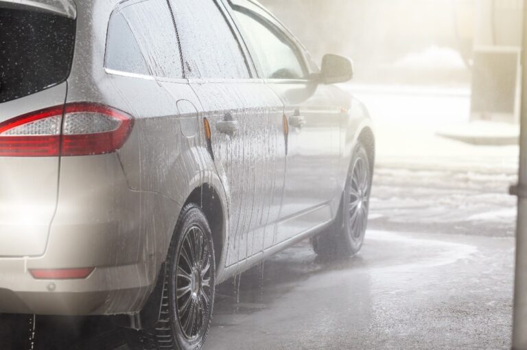 Rückansicht eines silbernen Autos, das in einer Autowaschanlage mit Wasser und Seife gewaschen wird