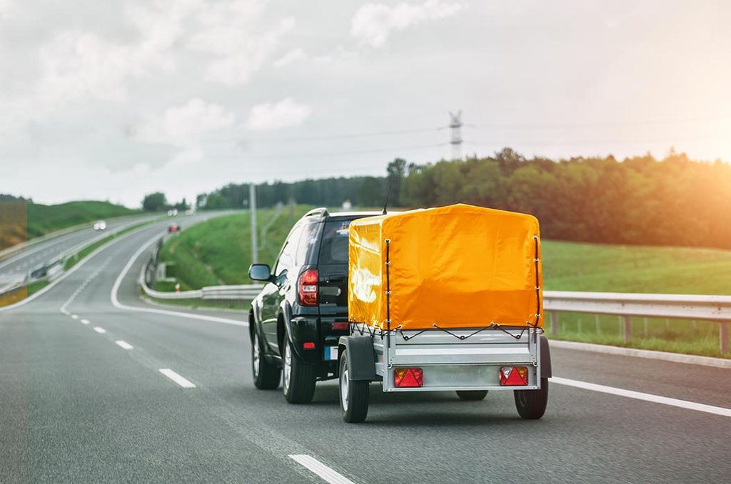 Schwarzes Auto zieht einen Anhänger mit orangefarbener Plane auf der Strasse
