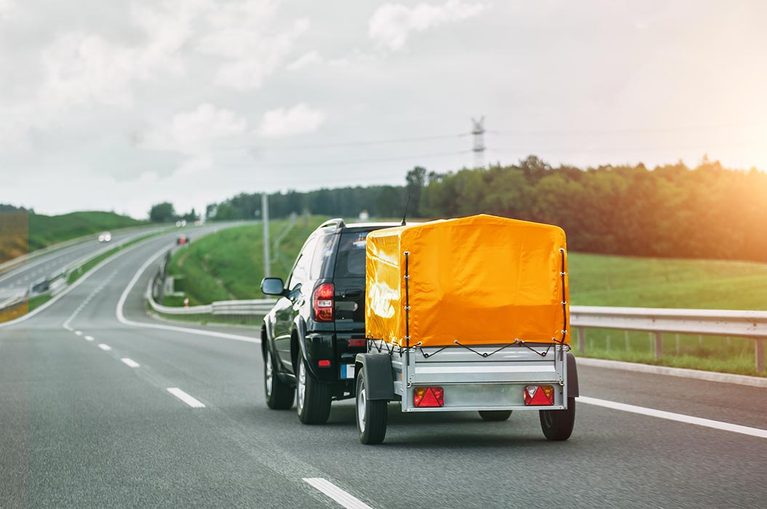 Schwarzes Auto zieht einen Anhaenger mit orangefarbener Plane auf der Strasse