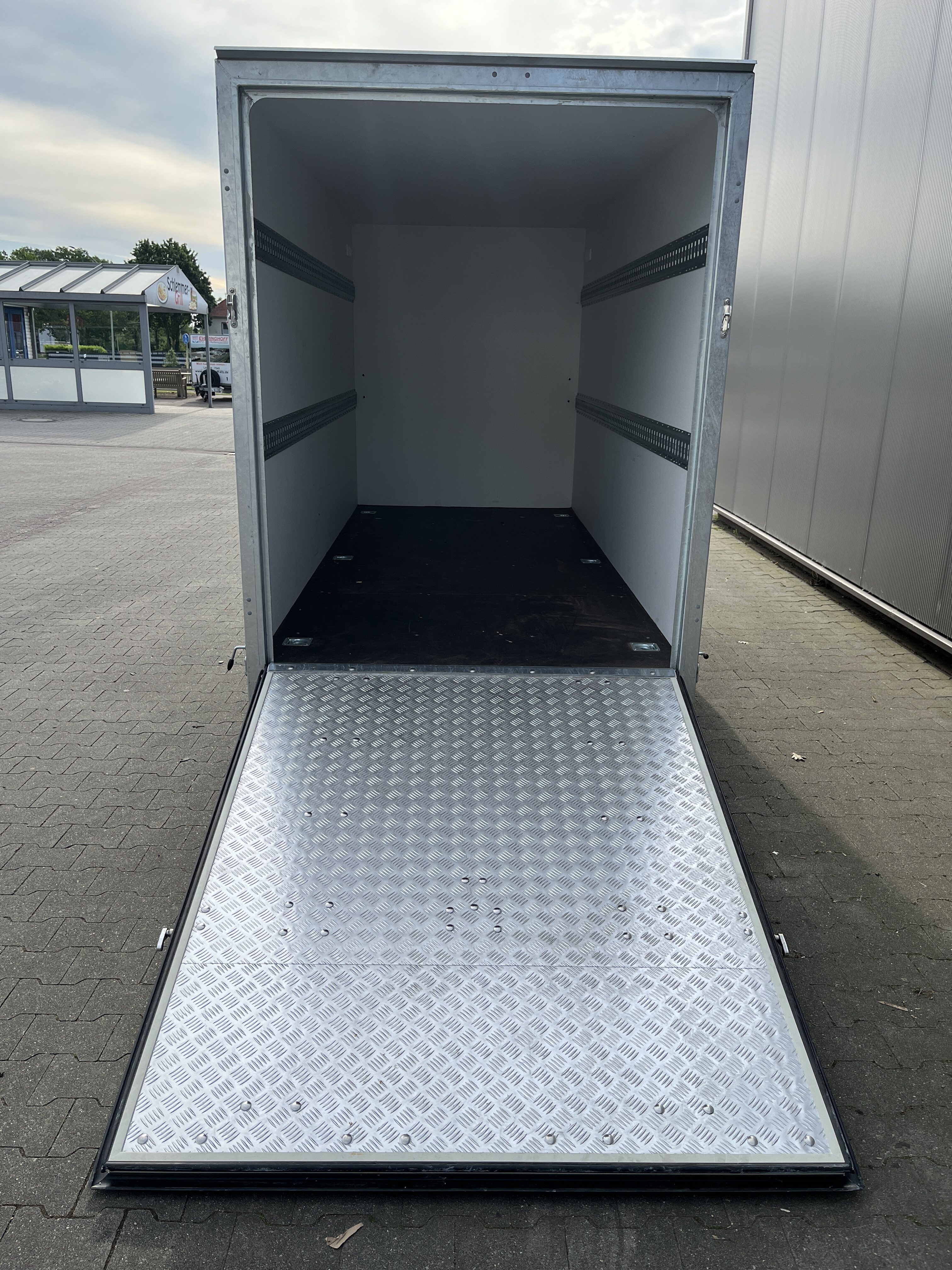 Geoeffneter weisser Kofferanhaenger mit heruntergelassener Riffelblech Auffahrrampe