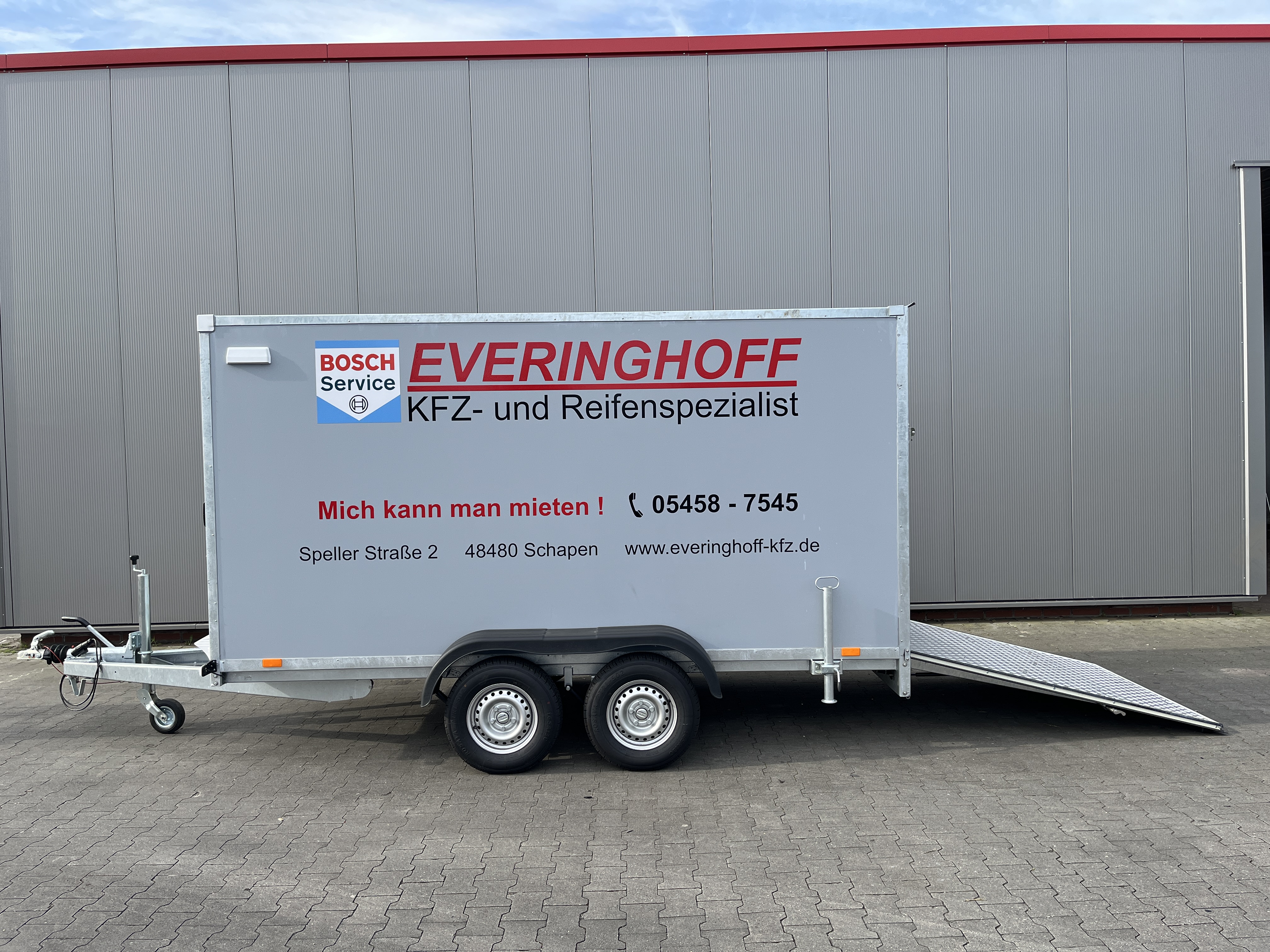 Grauer Kofferanhaenger von Everinghoff mit Rampe vor einer Halle zum Mieten